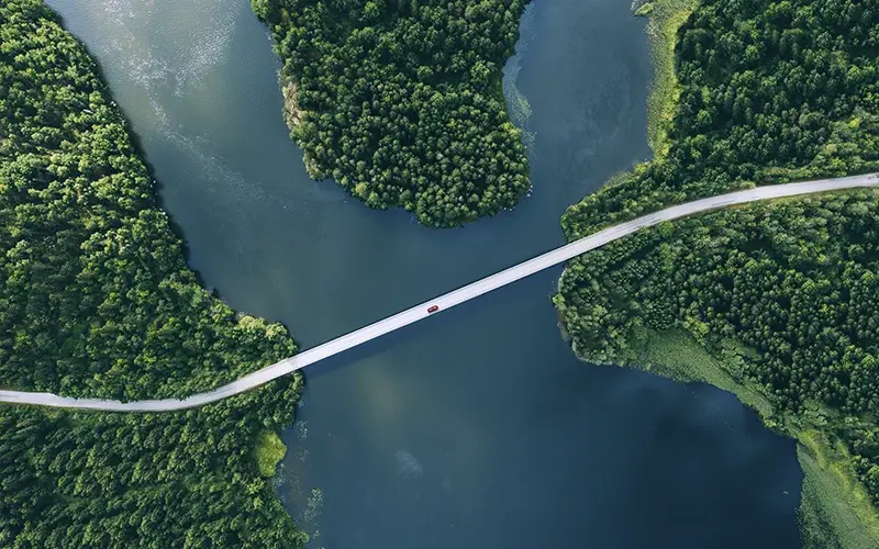 [Vogelperspektive rotes Fahrzeug auf Brücke über Fluss]